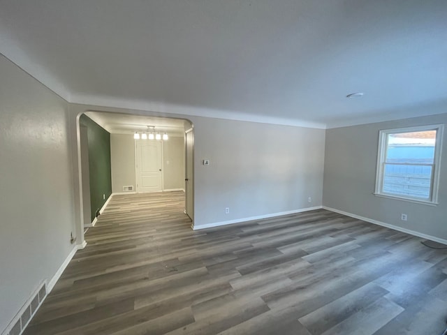 unfurnished room with baseboards, visible vents, arched walkways, and dark wood-type flooring