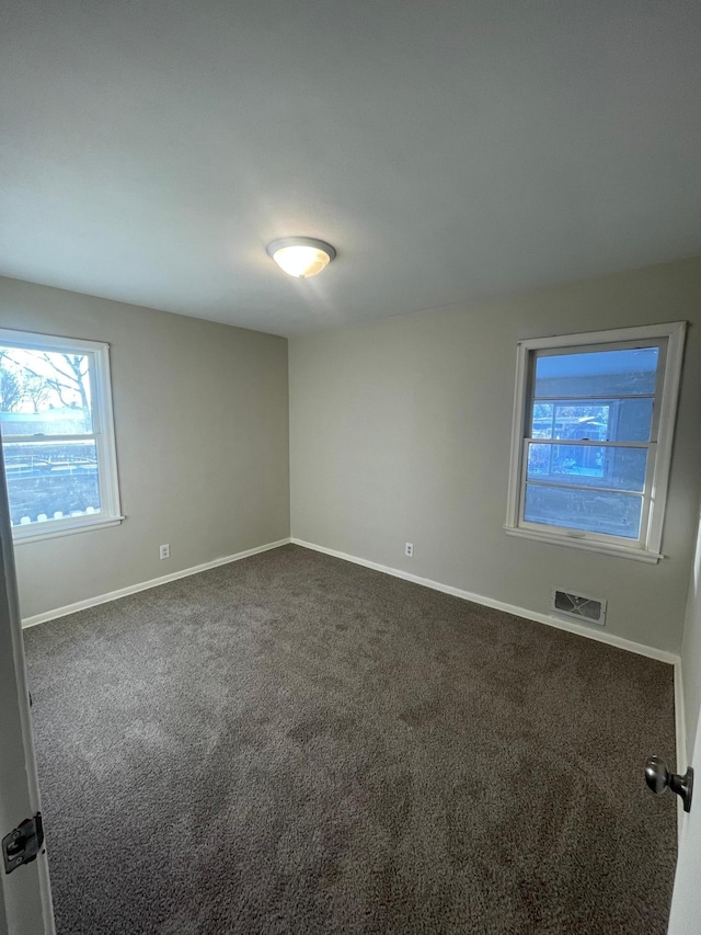 spare room featuring baseboards, visible vents, and dark carpet