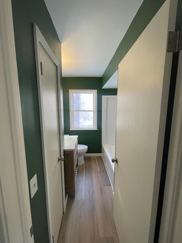 full bathroom featuring a washtub, toilet, vanity, wood finished floors, and baseboards