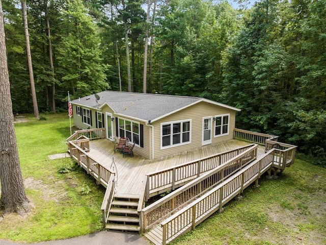 back of property featuring a forest view, a yard, roof with shingles, and a wooden deck