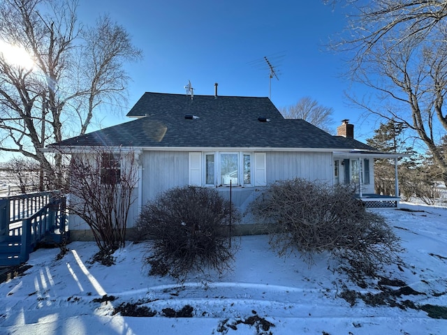 view of snowy exterior with a shingled roof, a chimney, and a garage