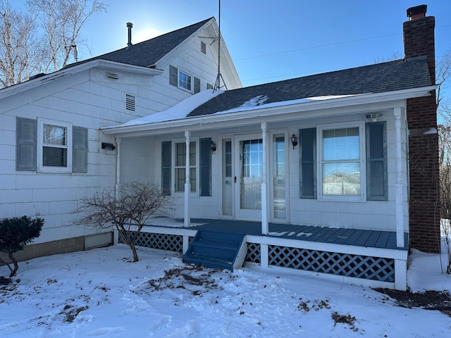 view of front of house with roof with shingles, a porch, a chimney, and brick siding