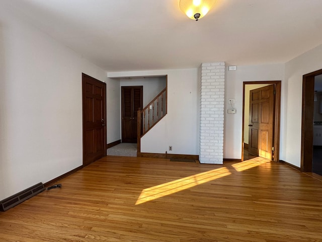 unfurnished room with light wood-type flooring, visible vents, baseboards, and stairs