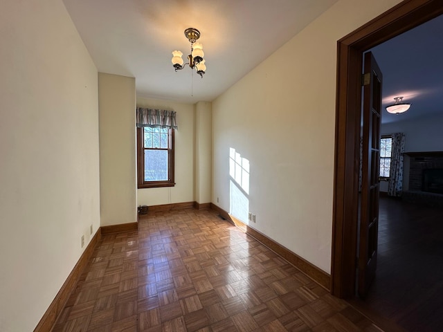 unfurnished room featuring a chandelier, a fireplace, and baseboards