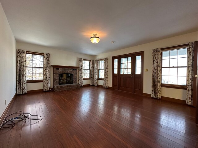 unfurnished living room with dark wood-style floors, a brick fireplace, baseboards, and a wealth of natural light