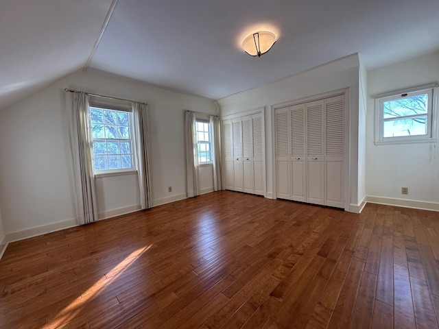 unfurnished bedroom with lofted ceiling, multiple closets, baseboards, and dark wood-type flooring