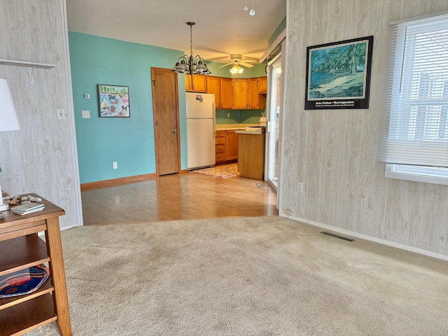 kitchen featuring baseboards, light carpet, freestanding refrigerator, visible vents, and brown cabinetry