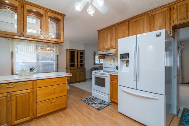 kitchen with white appliances, under cabinet range hood, light countertops, and brown cabinetry