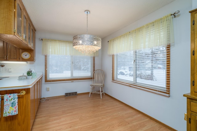 dining space featuring light wood finished floors, baseboards, visible vents, and a notable chandelier