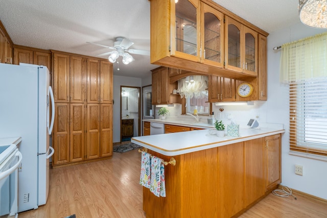 kitchen featuring white appliances, glass insert cabinets, brown cabinets, a peninsula, and light countertops