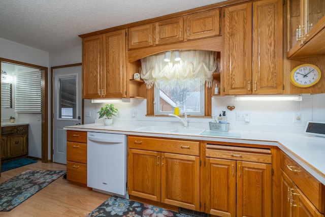 kitchen with white dishwasher, a sink, light countertops, light wood finished floors, and brown cabinetry