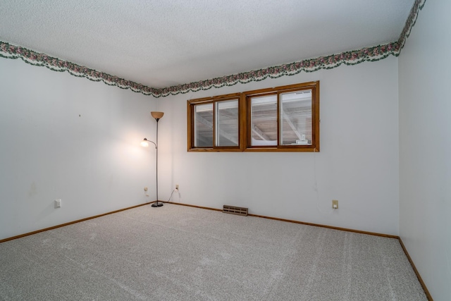 carpeted spare room featuring baseboards, visible vents, and a textured ceiling