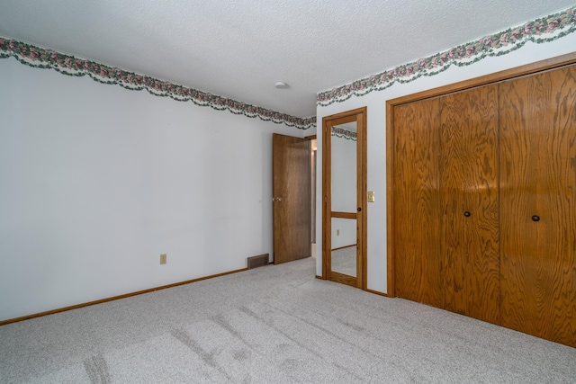 unfurnished bedroom with a closet, light carpet, a textured ceiling, and baseboards