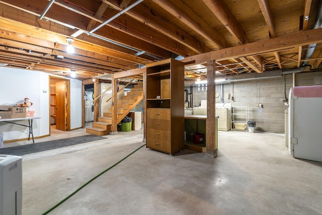 unfinished below grade area featuring concrete block wall, stairway, and washing machine and clothes dryer