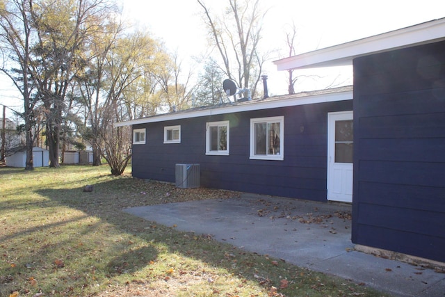 view of property exterior with an outbuilding, a yard, central AC unit, a patio area, and a shed