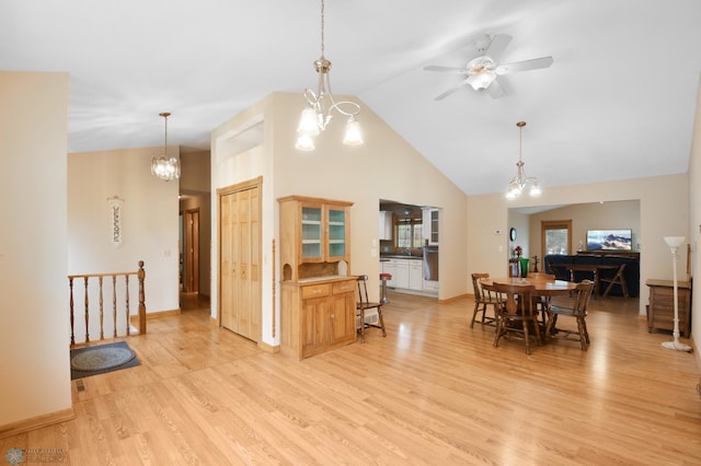 dining area with light wood finished floors, ceiling fan with notable chandelier, high vaulted ceiling, and baseboards