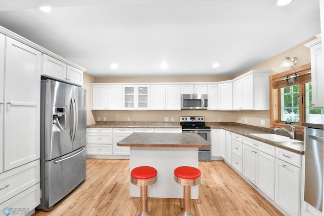 kitchen with light wood-style flooring, a sink, a center island, stainless steel appliances, and white cabinets