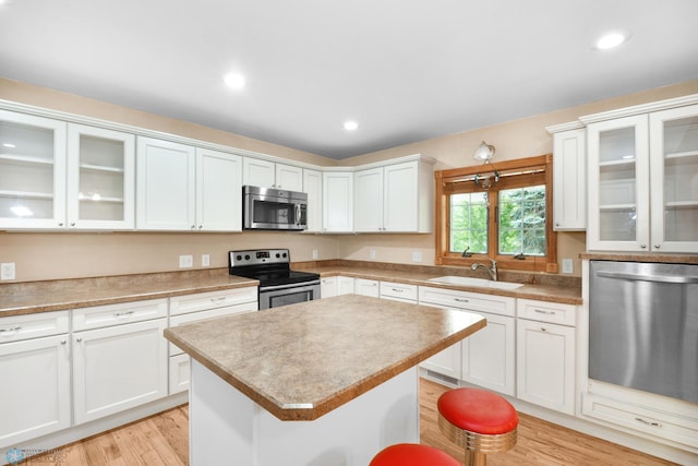 kitchen with a kitchen island, a sink, stainless steel appliances, white cabinetry, and light wood-type flooring