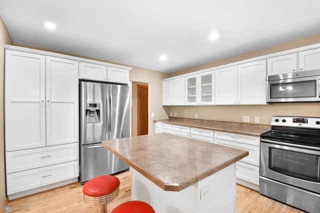 kitchen with light wood finished floors, a kitchen island, glass insert cabinets, stainless steel appliances, and white cabinetry