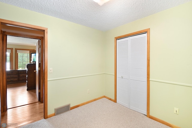 unfurnished bedroom with carpet, baseboards, visible vents, a closet, and a textured ceiling