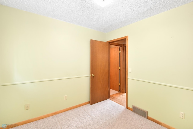 unfurnished room with visible vents, baseboards, carpet, and a textured ceiling