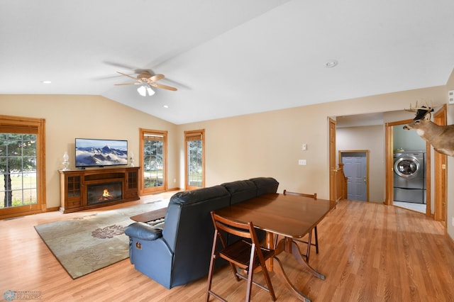 living room with lofted ceiling, light wood-style floors, a glass covered fireplace, washer / clothes dryer, and a ceiling fan