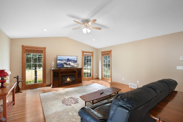 living room featuring a wealth of natural light, visible vents, a glass covered fireplace, and vaulted ceiling