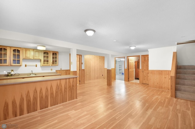 kitchen with light wood finished floors, a wainscoted wall, light countertops, and a sink