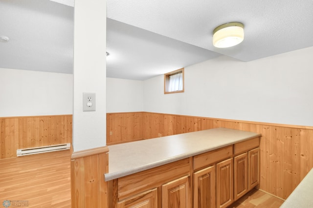 kitchen featuring a wainscoted wall, a baseboard heating unit, a textured ceiling, wood walls, and light countertops