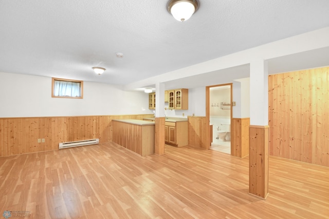 basement featuring a baseboard heating unit, a textured ceiling, wood walls, and wainscoting