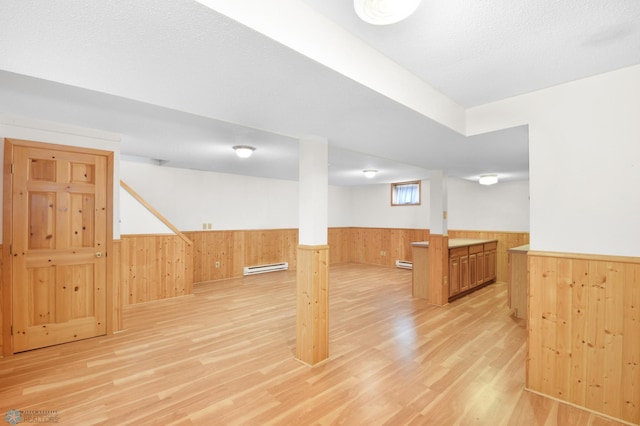 below grade area featuring light wood-type flooring, a wainscoted wall, wooden walls, and a baseboard radiator