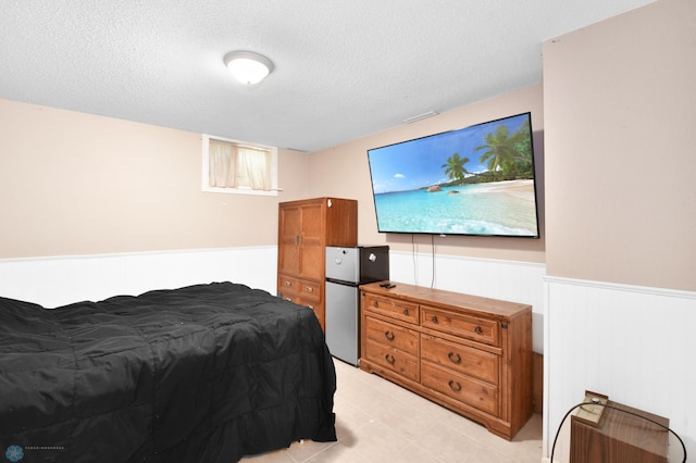 bedroom featuring a wainscoted wall, a textured ceiling, and freestanding refrigerator