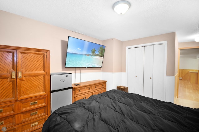 bedroom with a textured ceiling, a closet, freestanding refrigerator, and wainscoting