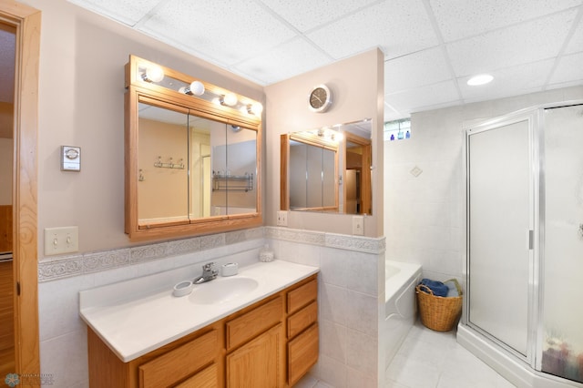 bathroom with a paneled ceiling, tile walls, a stall shower, and vanity