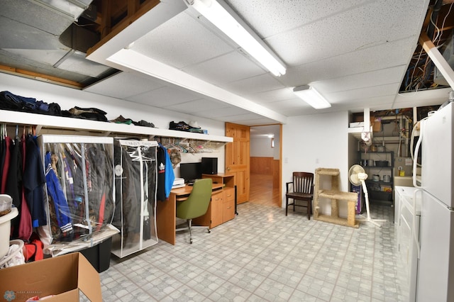 finished basement featuring tile patterned floors, a drop ceiling, and freestanding refrigerator