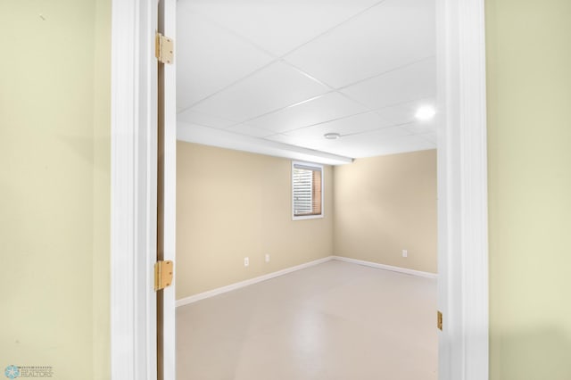 basement with a paneled ceiling and baseboards