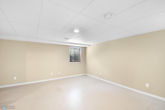 unfurnished room with finished concrete flooring, baseboards, and a drop ceiling