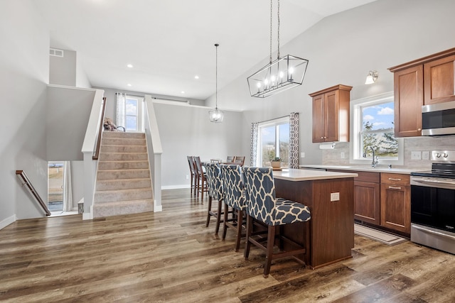 9764 Saint Andrews Dr, Elko New Market, MN 55020 - kitchen featuring appliances with stainless steel finishes, a kitchen island, plenty of natural light, brown cabinets, and high vaulted ceiling