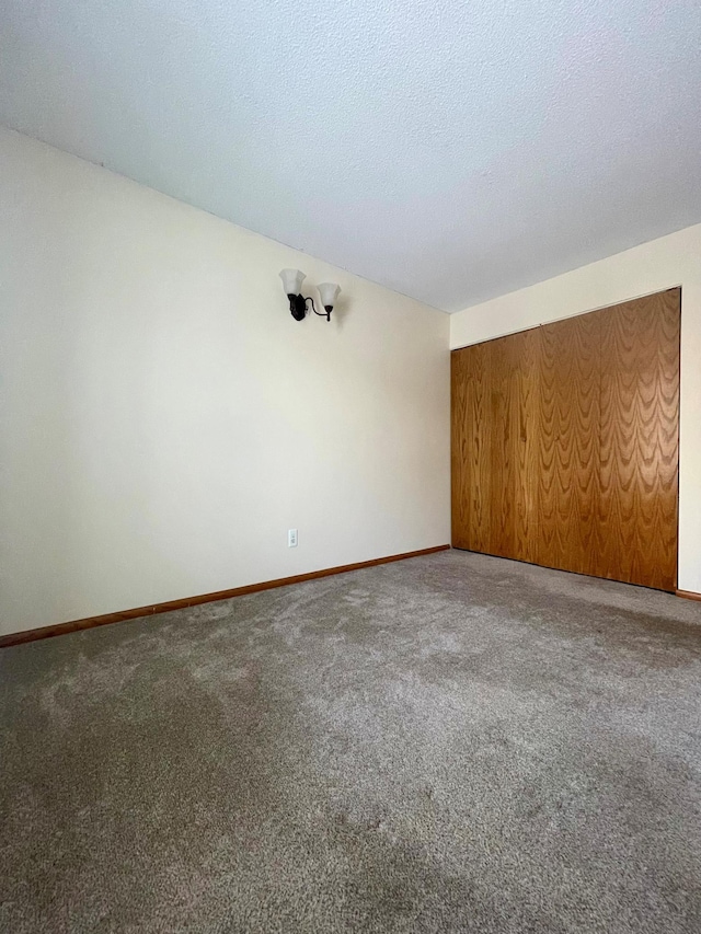 carpeted empty room with a textured ceiling and baseboards