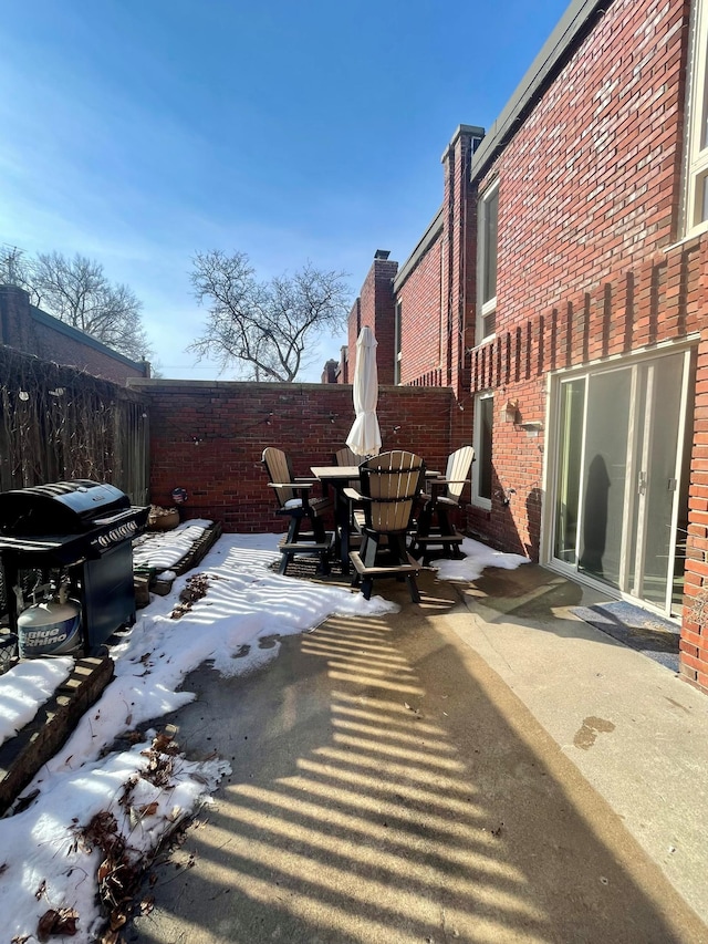 snow covered patio featuring outdoor dining space, area for grilling, and a fenced backyard