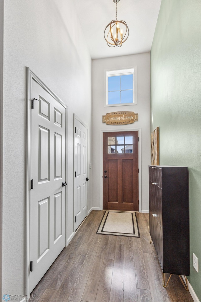 foyer entrance with a towering ceiling, a notable chandelier, baseboards, and wood finished floors