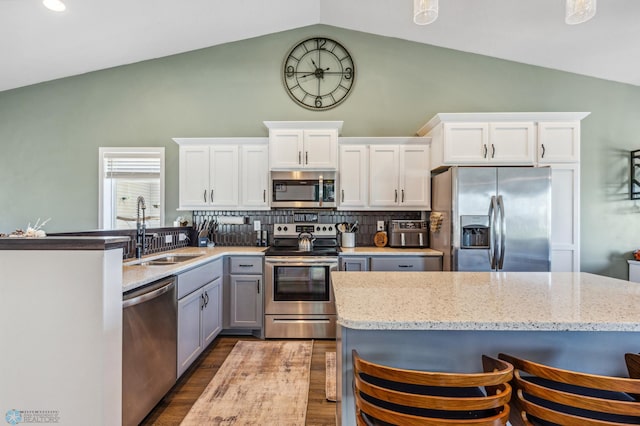 kitchen featuring tasteful backsplash, vaulted ceiling, stainless steel appliances, white cabinetry, and a sink