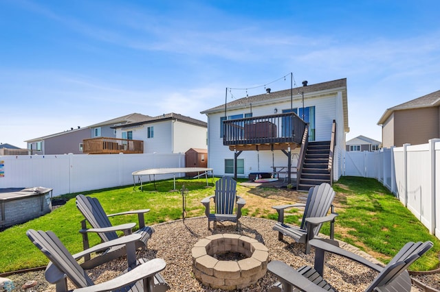 rear view of house with a fire pit, a fenced backyard, stairway, a trampoline, and a deck