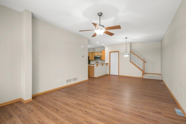 unfurnished living room with a ceiling fan, light wood-type flooring, visible vents, and stairs