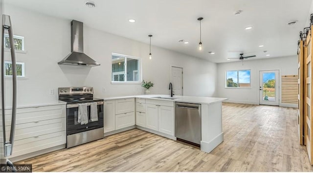 kitchen featuring white cabinets, open floor plan, wall chimney range hood, appliances with stainless steel finishes, and decorative light fixtures