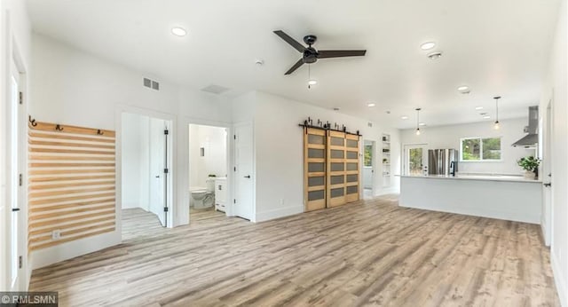 unfurnished living room with a barn door, visible vents, ceiling fan, light wood-style flooring, and recessed lighting