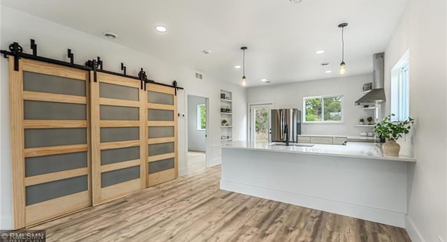 kitchen featuring freestanding refrigerator, decorative light fixtures, wall chimney range hood, and a barn door