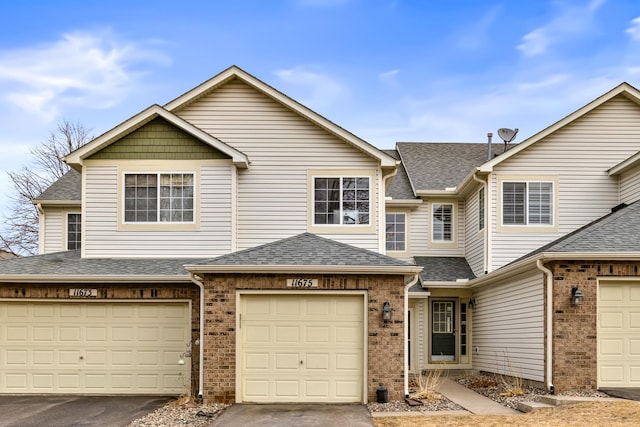 townhome / multi-family property with brick siding, an attached garage, and roof with shingles