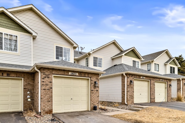 townhome / multi-family property featuring a shingled roof, brick siding, and a garage