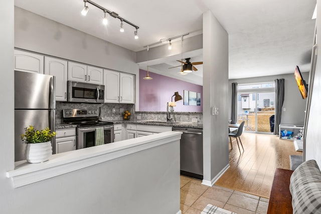 kitchen featuring appliances with stainless steel finishes, backsplash, a peninsula, white cabinetry, and a sink